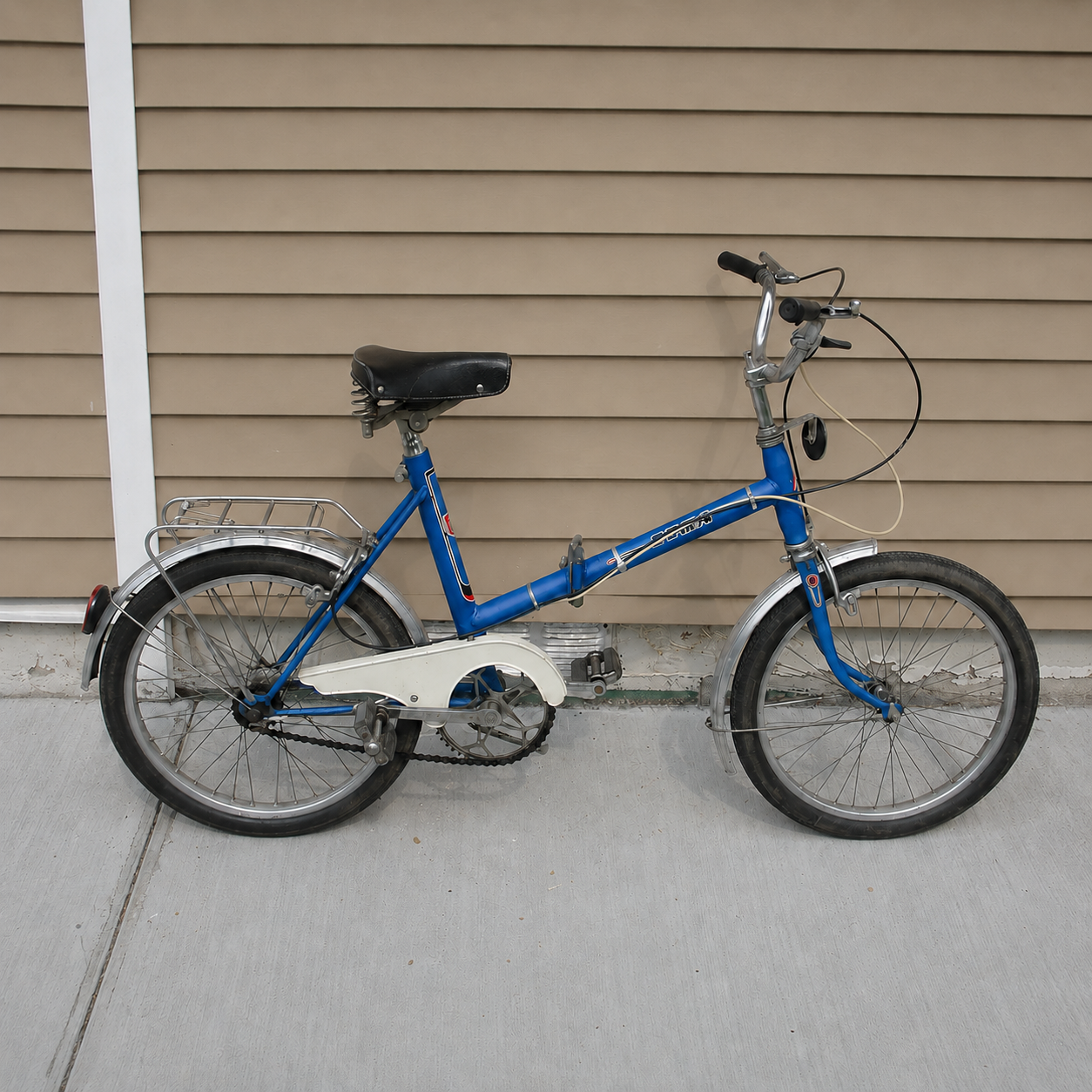 Vintage blue step-through city bike with small wheels, chrome fenders, rear rack, and upright handlebars. Vintage blue step-through city bike with small wheels, chrome fenders, rear rack, and upright handlebars.